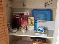 White shelf with scrapbooking supplies including decorative punches, decorative trimmer, rotary cutter, and packages of scrapbooking paper and embellishments.