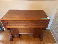 Front view of the wooden spinet desk showing the closed hinged top, carved legs, and panel details
