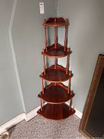 Full view of the 5-tier wooden corner shelf standing against a grey wall in a carpeted room.