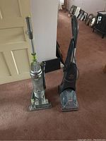 Two upright vacuum cleaners side by side on carpet: a Bissell Air and a Shark Navigator.