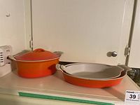 Oval orange enameled casserole with lid and shallow oval dish on countertop