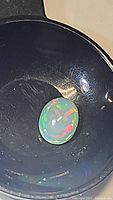 Close-up image of a single oval-shaped Ethiopian opal gemstone showing vibrant rainbow flash colors on a milky base, placed inside a dark circular container for viewing.