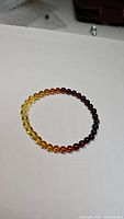 Stretchy bracelet composed of small round Baltic amber beads showing smooth gradient from yellow to dark brown on white background.