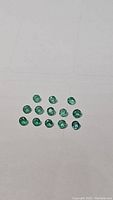 15 small polished round and oval emerald gemstones arranged on a flat surface, showing green color and luster under neutral lighting.