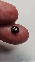 Close-up photo of a natural black star sapphire round cabochon gemstone held between fingers showing the star effect on the surface.