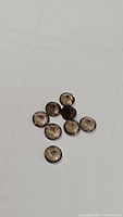 Eight round faceted smokey quartz gemstones with good clarity and diamond cut, laid out on white surface.
