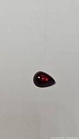 Pear-shaped cherry red garnet cabochon on white background, showing gemstone's color and clarity from above.
