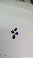Four deep purple natural oval cabochon amethyst gemstones arranged on a white surface, showing color and size comparison.