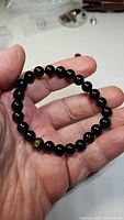 Hand holding a black bead stretchy bracelet with one gold sheen obsidian bead visible.