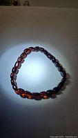 Top view of the Baltic amber bracelet showing its smooth, translucent dark reddish-brown oval beads arranged in a circular formation.