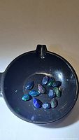 Eleven pear cut calibrated Ethiopian black opals displayed in a black bowl under neutral light showing bright multicolored flashes of red, green, and blue.