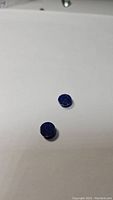Two small round lapis lazuli cabochon gemstones on white background, showing dark blue color and polished domed shape.