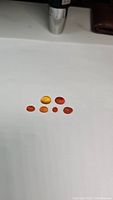 Seven mixed-shape mandarin orange carnelian cabochons arranged on a white background, showing color variations and surface polish.