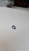 Oval cut pink purple amethyst gemstone on white background, showing light reflection and transparency.