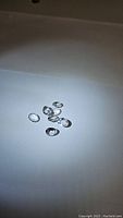 Seven clear oval faceted natural crystal quartz gemstones spread on white surface under lighting, showing clarity and sparkle.
