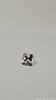 Square fancy cut natural green amethyst gemstone shown from top angle against grey background.