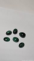 Seven polished natural malachite gemstones laid out on a white background, showing deep green color and banded patterns.