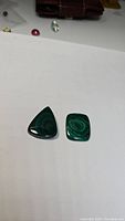 Two natural malachite cabochons on white background, clearly showing the triangular and square shapes and the distinctive green banding of the stones.