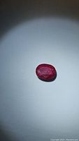 Oval cut red ruby gemstone with opaque quality under spotlight.