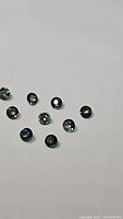 Lot of 10 small round-cut natural sapphires showing bi-colored blue, yellow, and green hues.