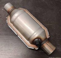 Full view of steel catalytic converter showing cylindrical body, welded seams, and pipe ends.