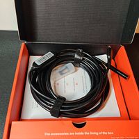 The borescope camera cable coiled inside an orange and black box with some documents underneath.