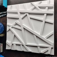 Close-up of one white 3D wall tile featuring intersecting angular linear raised designs.