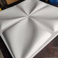 Close-up angled photo of a single white 3D wall panel tile showing a concave geometric design with four sections.