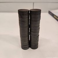 Stacked button magnets showing height and uniformity, dark matte finish typical of ferrite.