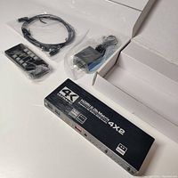 4K 60Hz 4x2 HDMI matrix switch device with included remote, power adapter, and HDMI cable in plastic bags alongside empty product box.
