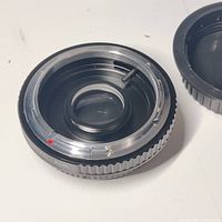 Top and inner view of black metal Canon FD to EOS lens adapter showing brass and aluminum construction with a red orientation marker.