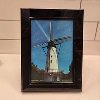 Front view of the black photo frame showing a photo of a windmill, glossy finish.