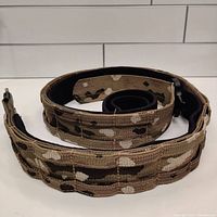 Rolled camouflage tactical belt showing woven material and modular webbing for attachments.