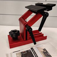 Side view of the metal tool sharpening jig showing the red base and black adjustable clamps.