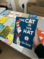Photo of The Cat in the Hat book held showing front cover and other books on table.