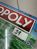 Close-up of Monopoly logo on the box showing the red and white Monopoly branding with money graphics and a sticker numbered 39.