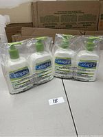 Four bottles of Cetaphil lotion in clear plastic packaging on a table.