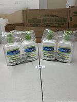 Four bottles of Cetaphil DailyAdvance Ultra Hydrating Lotion packaged in two sets of two bottles each sealed in clear plastic with green pump tops visible, placed on a white table with a cardboard background.