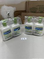 Four bottles of Cetaphil DailyAdvance Lotion in two sets of two, wrapped in clear plastic on a table with cardboard background.