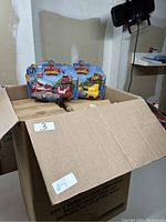Opened cardboard box containing several brand new Spin Master Mighty Express train toys still in packaging with visible characters Rescue Red and Rocky.