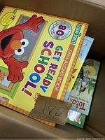 Photo showing box containing 'Sesame Street Get Ready for School' sing-along book and other books including 'Toto's My Amazing Adventure'.