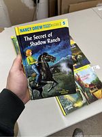 Close-up photo of 'The Secret of Shadow Ranch' book held in a hand showing cover art and title