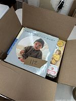 Photo showing an open box containing 'Knitting for Baby' and other parenting books stacked inside.