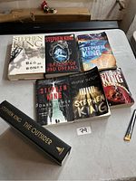 Top view of seven Stephen King books arranged on a table including Bag of Bones, Bazaar of Bad Dreams, Duma Key, The Outsider, The Dark Tower: The Drawing of the Three, Different Seasons, and Desperation.