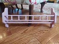 Photo of light pink painted wooden wall shelf with spindled railing on hardwood floor showing front view