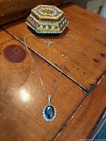 Photo showing pendant on chain and decorative container on wooden surface