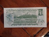 Reverse side of the 1973 Canadian one dollar bill showing Parliament Hill, a tugboat, and a log boom scene with values 1, ONE, and UN.