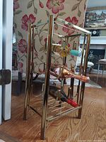Angled side view of solid brass bottle rack on wooden floor, displaying the rack's polished brass finish and slots for holding bottles horizontally.