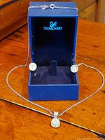 Swarovski blue box with earrings and pendant displayed on wooden surface. The pendant is hanging on the 16-inch silver chain, with earrings placed inside the box.