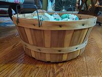 Photo of large rustic wooden apple basket with metal wire handles on hardwood floor